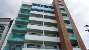 Un edificio de varios pisos con un diseño arquitectónico moderno, que destaca por una sección vertical y varios balcones con barandillas de vidrio.