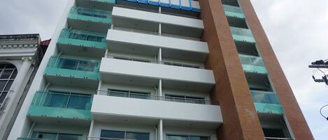 A multi-story building with a modern architectural design, featuring a prominent vertical section and multiple balconies with glass railings.