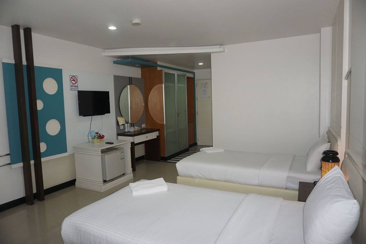 Ein Hotelzimmer mit zwei Betten, einem Schreibtisch mit Spiegel, einem Fernseher und einem Badezimmer mit Dusche.