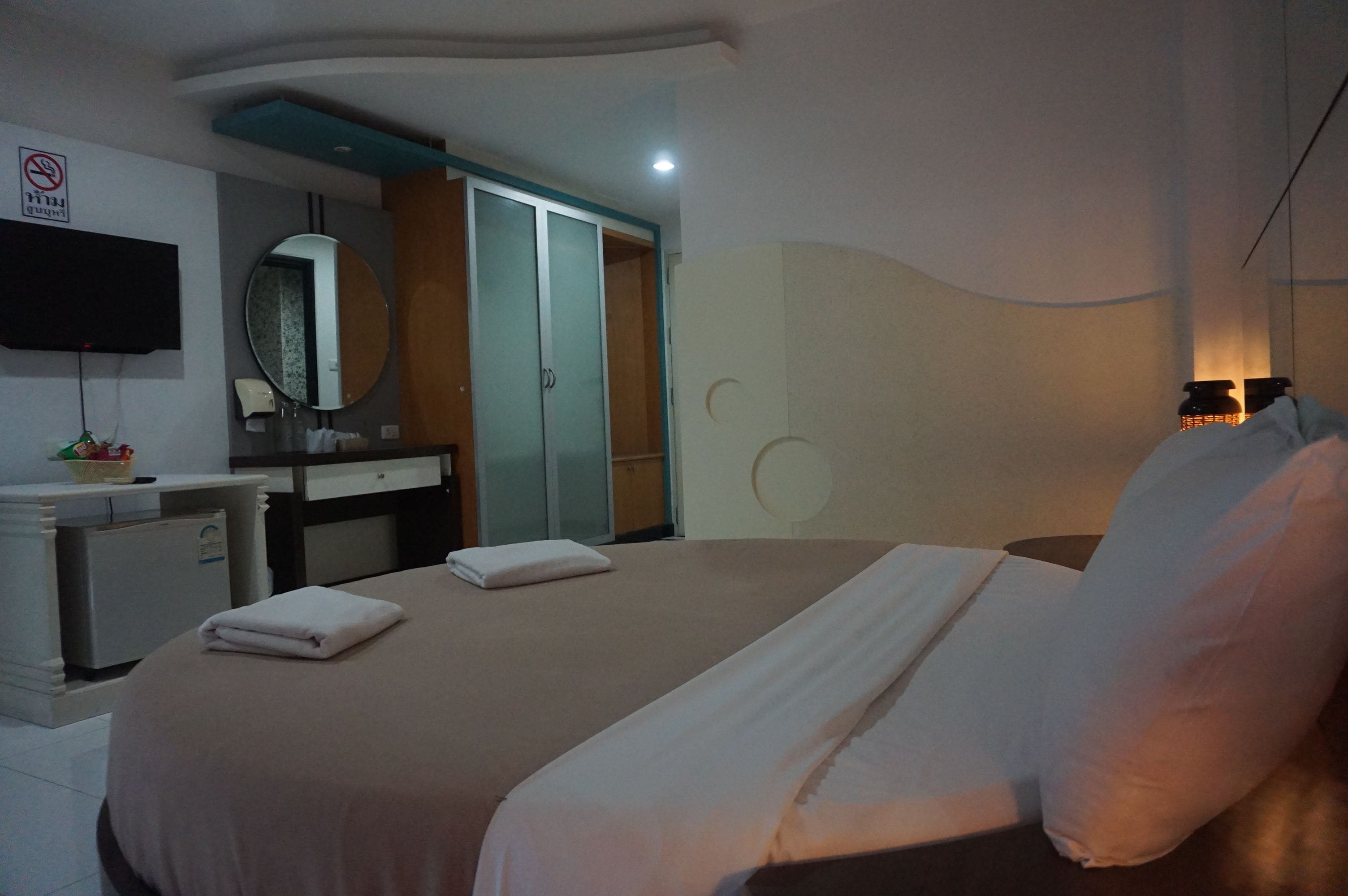 A hotel room with a bed, a desk with a mirror, a wardrobe, and a television on the wall.