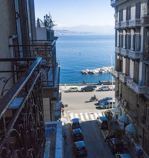 A coastal street view with buildings, parked cars, and a clear view of the sea. - Di Palma Suite (Naples)