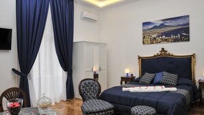 A bedroom with a large bed, a chair, a table with a glass vase, and a painting on the wall. - Di Palma Suite (Naples)