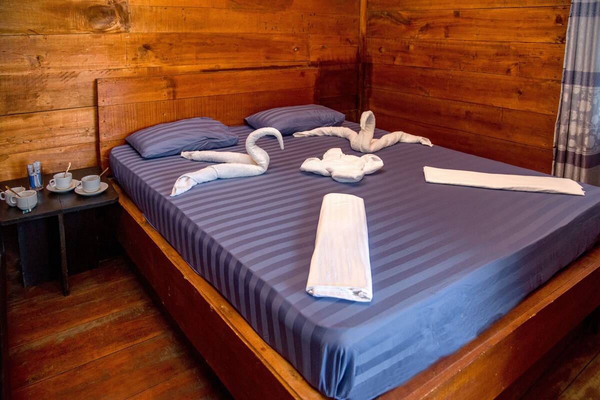 A wooden cabin room with a bed, pillows, and towels arranged on the bed.