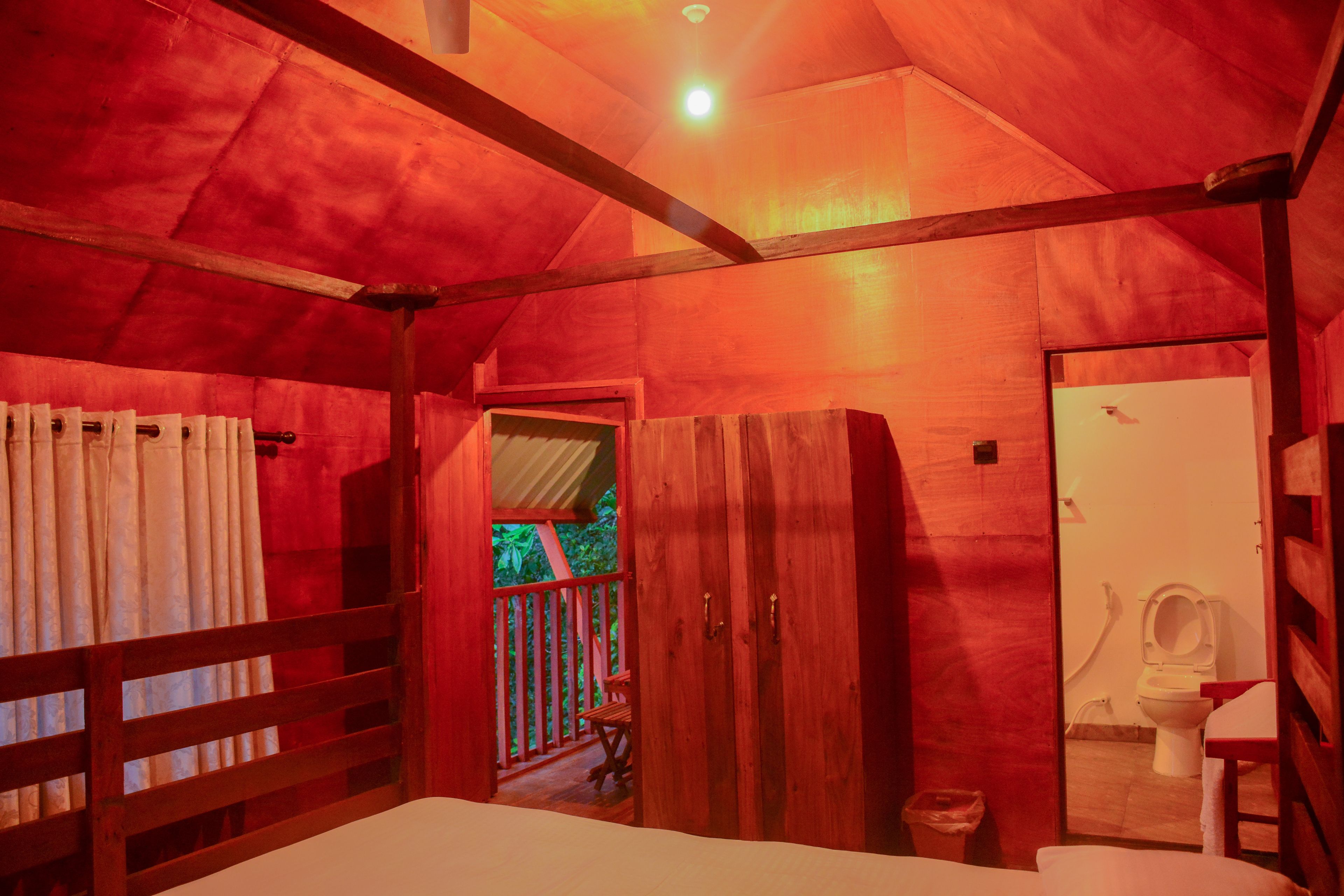 Een houten kamer met een bed, een deur naar een badkamer en een klein balkon met een stoel.