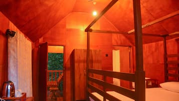 Un dormitorio acogedor en el ático con una cama nido de madera, una mesita con un hervidor y una puerta que da a un balcón con vistas a la vegetación.