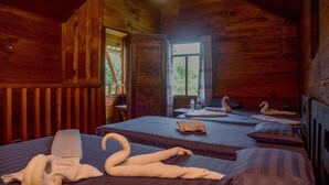 A wooden cabin room with two beds, a window, and a door leading outside.