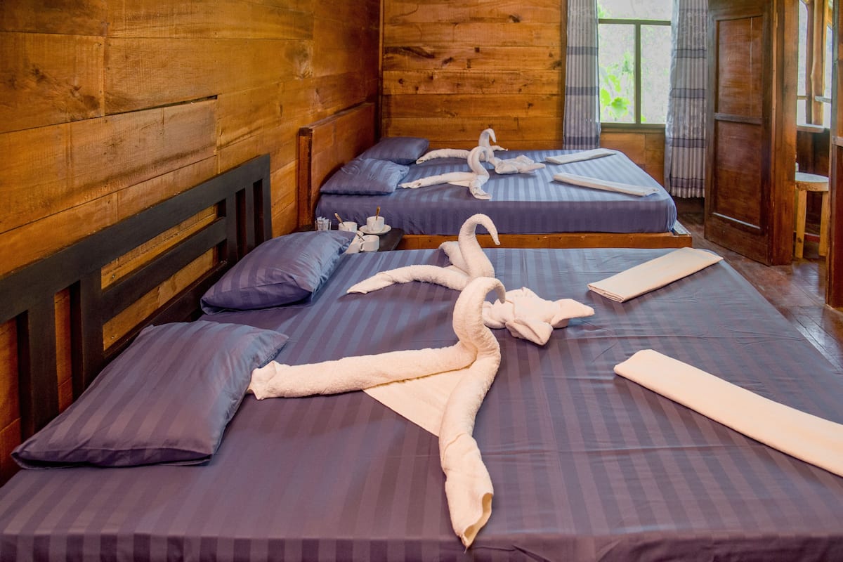 A wooden cabin room with two beds, each with purple bedding and white towels arranged in a swan shape.