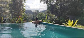 A person relaxing in a clear pool surrounded by lush greenery. - Sinharaja Forest Gate (Deniyaya)