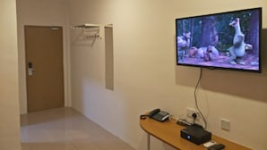 A hotel hallway with a TV mounted on the wall displaying an animated movie scene, a telephone, and a remote control on a wooden table. - Anderson Hotel (Ipoh)