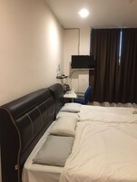 A hotel room with a large bed, a black sofa, a desk with a computer, and a TV mounted on the wall.