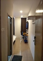 Habitación de hotel con cama, escritorio, silla, televisor y baño con ducha.