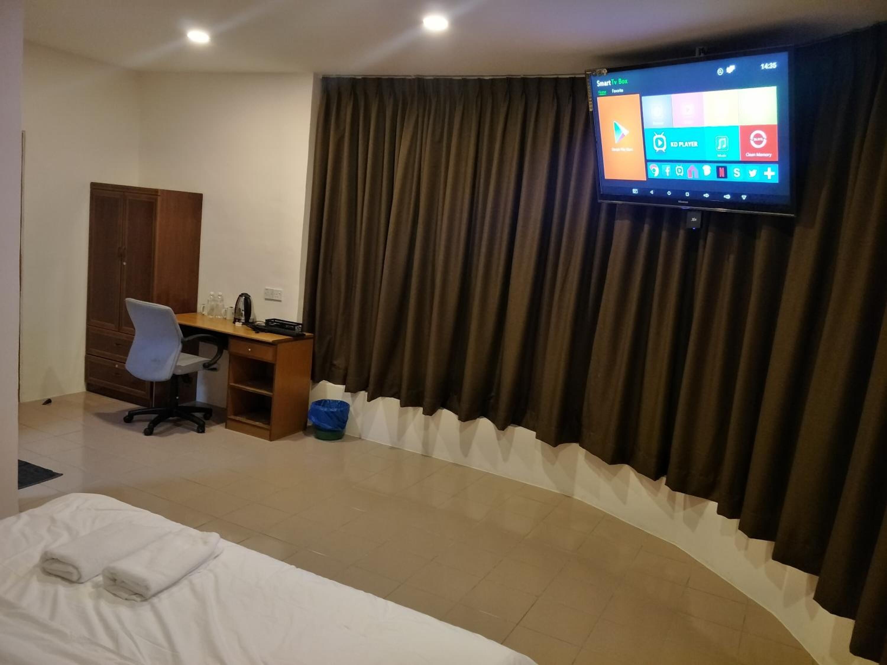 Een hotelkamer met een bed, een bureau met een computer, een stoel, een aan de muur bevestigde televisie en een gordijn.