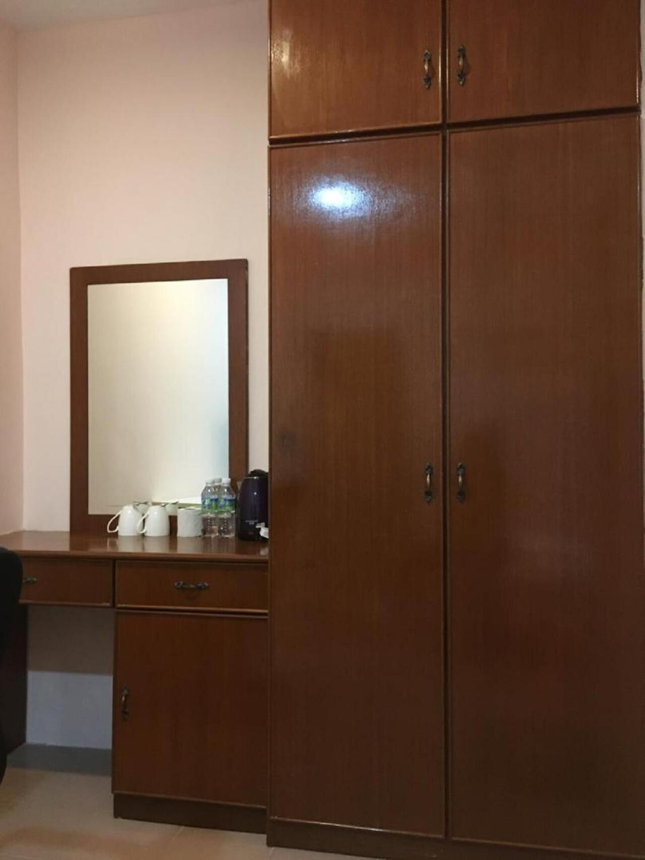 A wooden wardrobe with a mirror and a desk with a kettle, cups, and a water bottle.