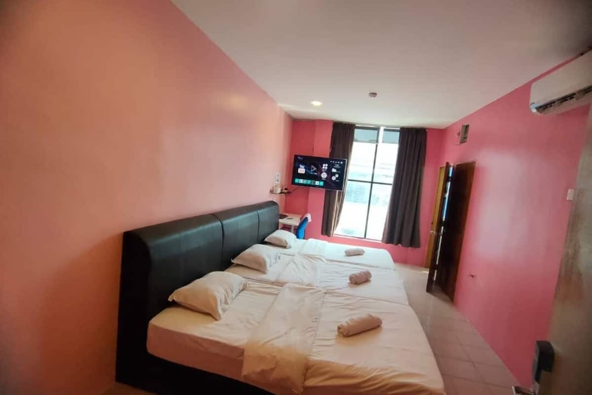 A hotel room with a large bed, a flat-screen TV mounted on the wall, and a window with curtains.