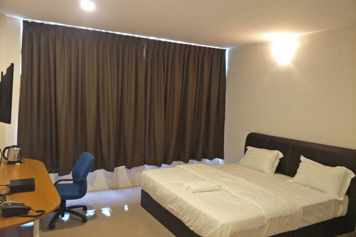 A hotel room with a bed, a desk with a chair, and a large window with curtains.