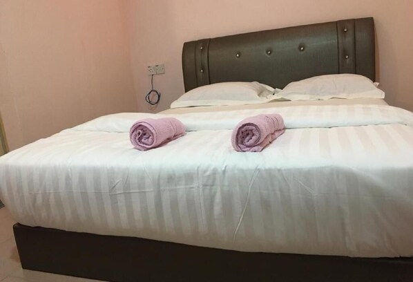 Una cama bien tendida con ropa blanca y dos toallas enrolladas encima.