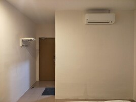 Un pasillo con un equipo de aire acondicionado blanco montado en la pared, una puerta al final y un tapete pequeño en el suelo.