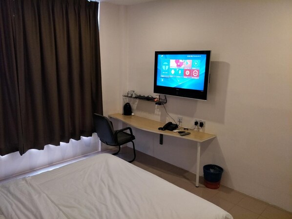 A hotel room with a bed, a desk with a computer monitor, a chair, and a coffee maker.