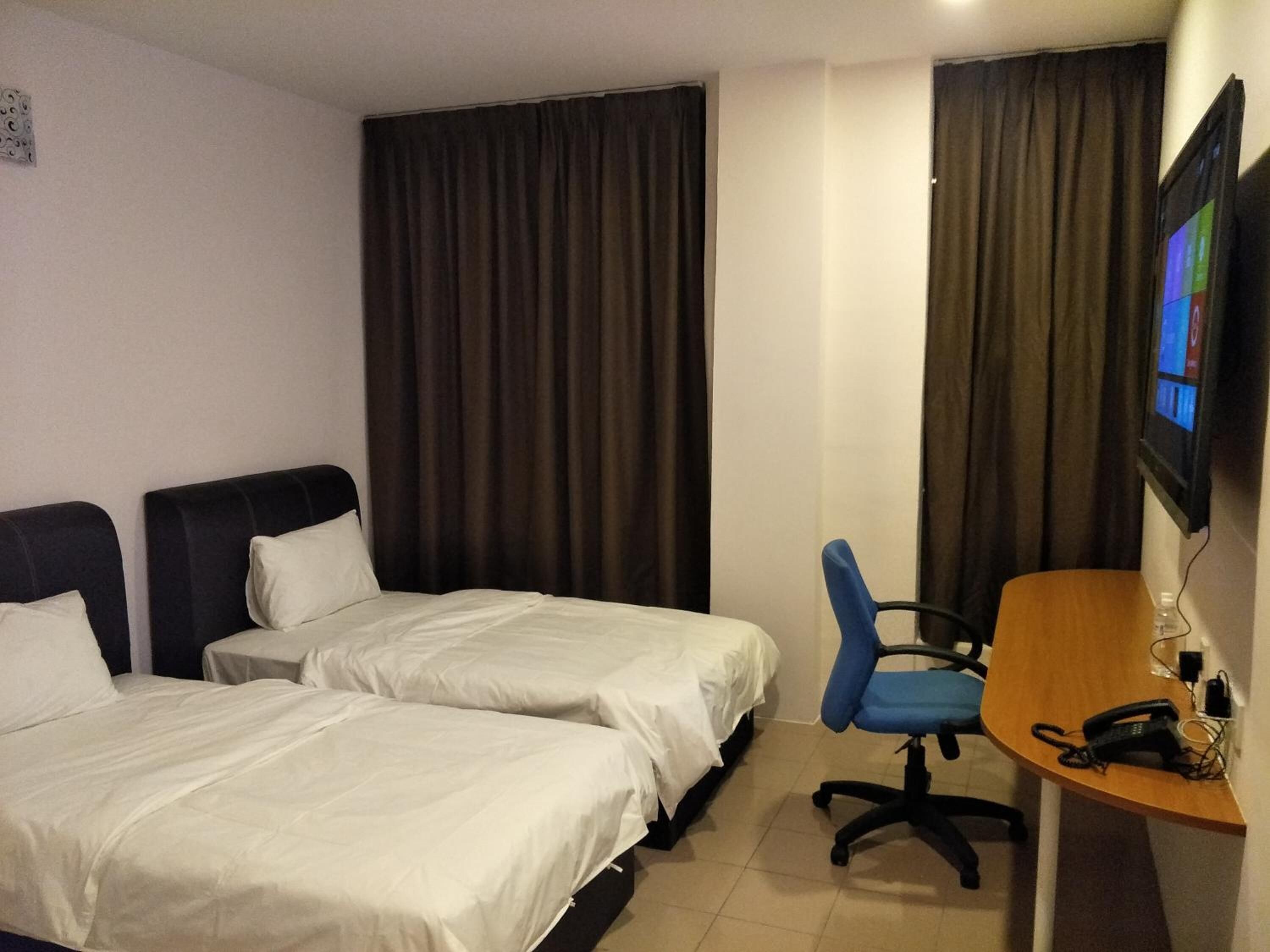 A hotel room with two beds, a desk, a chair, a TV, and a telephone.