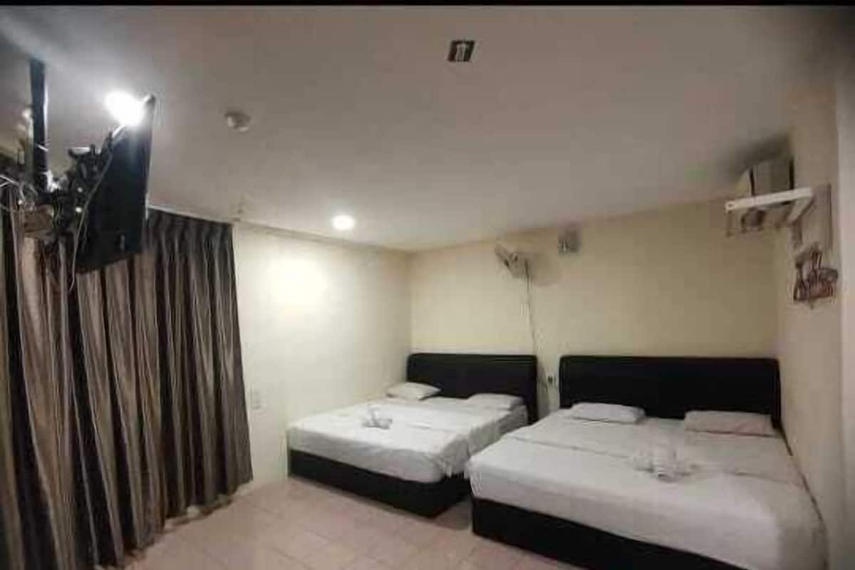 A hotel room with two single beds, a flat-screen TV, a ceiling fan, and a window with curtains.