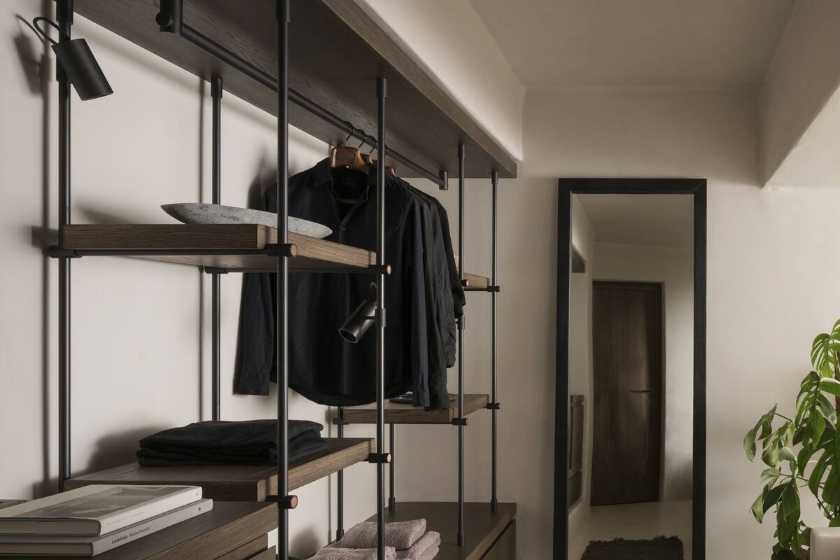 Una habitación moderna y minimalista con una estantería de madera empotrada, un espejo y una planta en maceta.