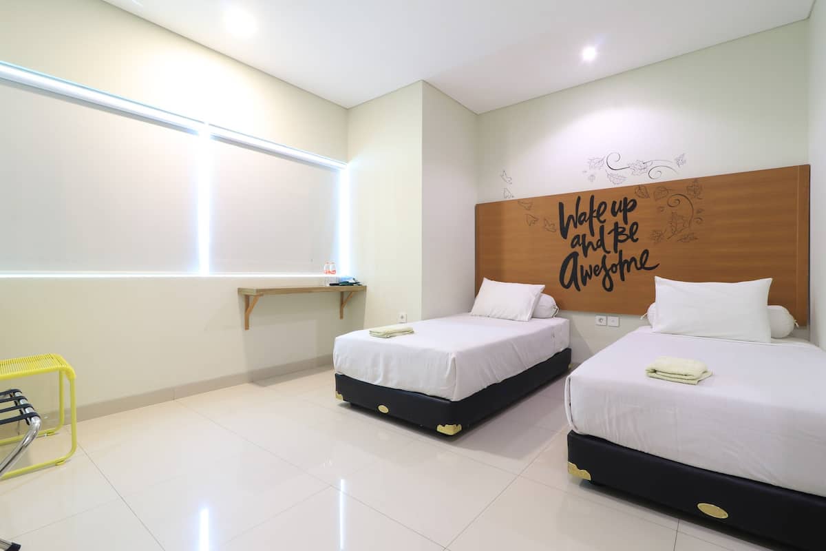 A hotel room with two beds, a desk, a chair, and a motivational wall art.
