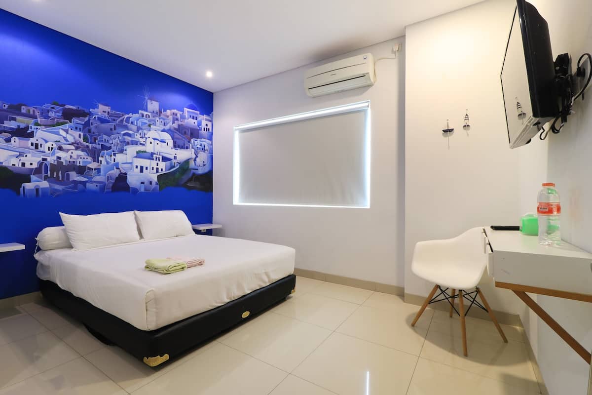 A modern bedroom with a bed, a desk, and a chair. There is a wall-mounted air conditioner and a window with blinds.
