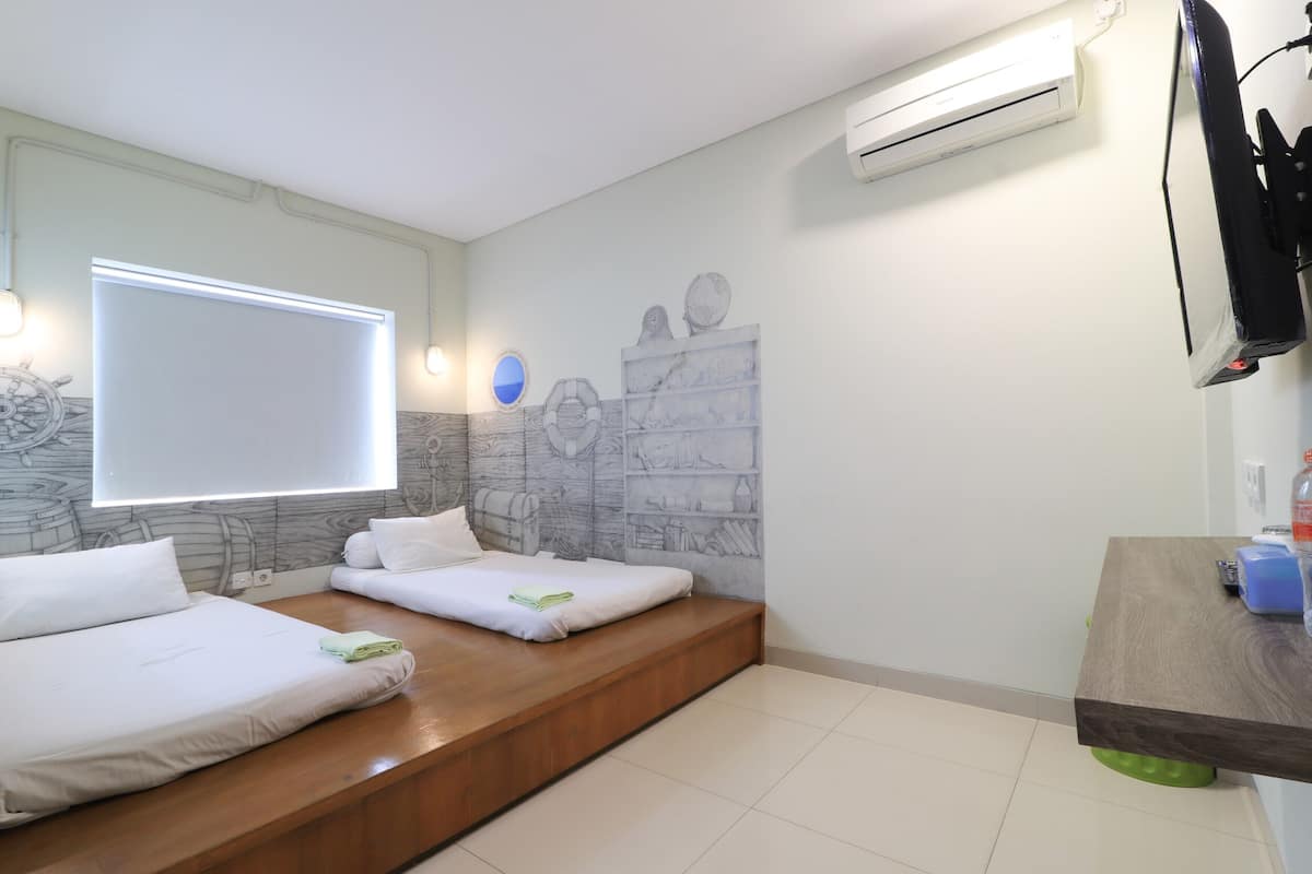 A hotel room with two beds, a large window, an air conditioner, and a wooden bench.