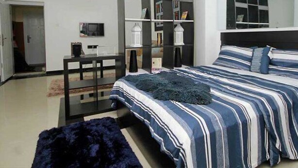 A modern bedroom with a large bed, a desk, and a bookshelf. - Capital & County Apartment Ikate (Lekki)