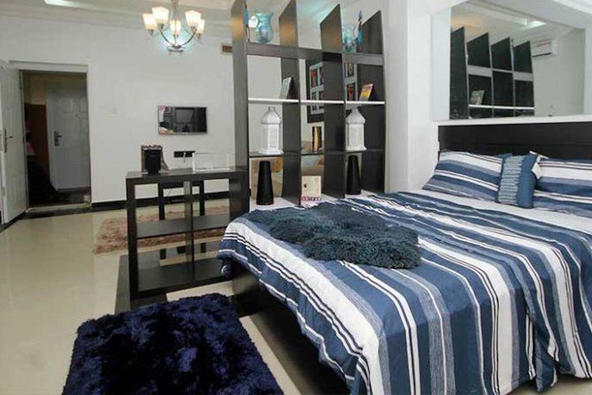 A modern bedroom with a large bed, a desk, and a bookshelf.