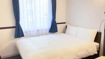 A hotel room with a bed, a bedside table, a lamp, and a window with curtains.