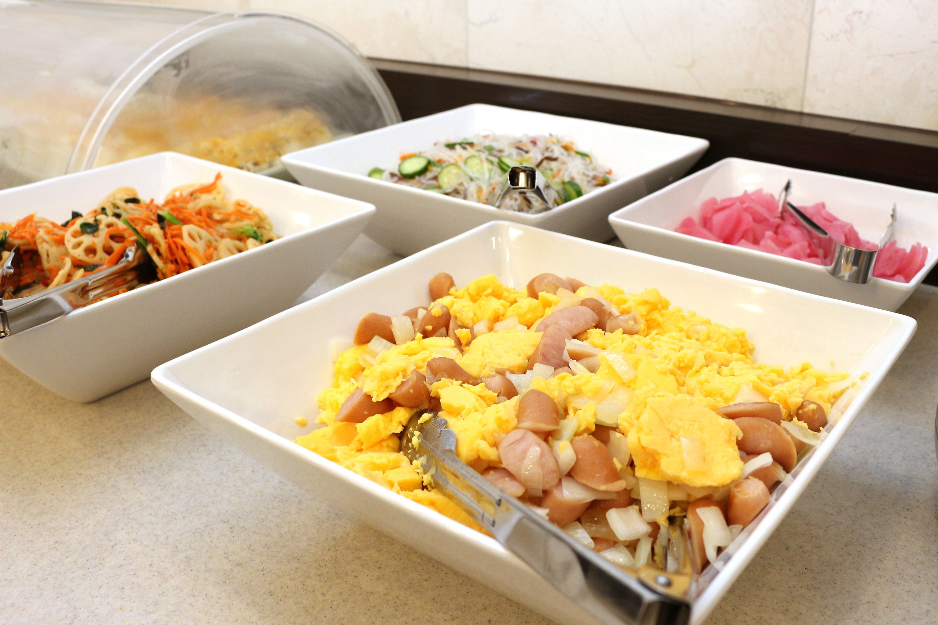 A buffet table with various dishes including noodles, scrambled eggs, and a salad.