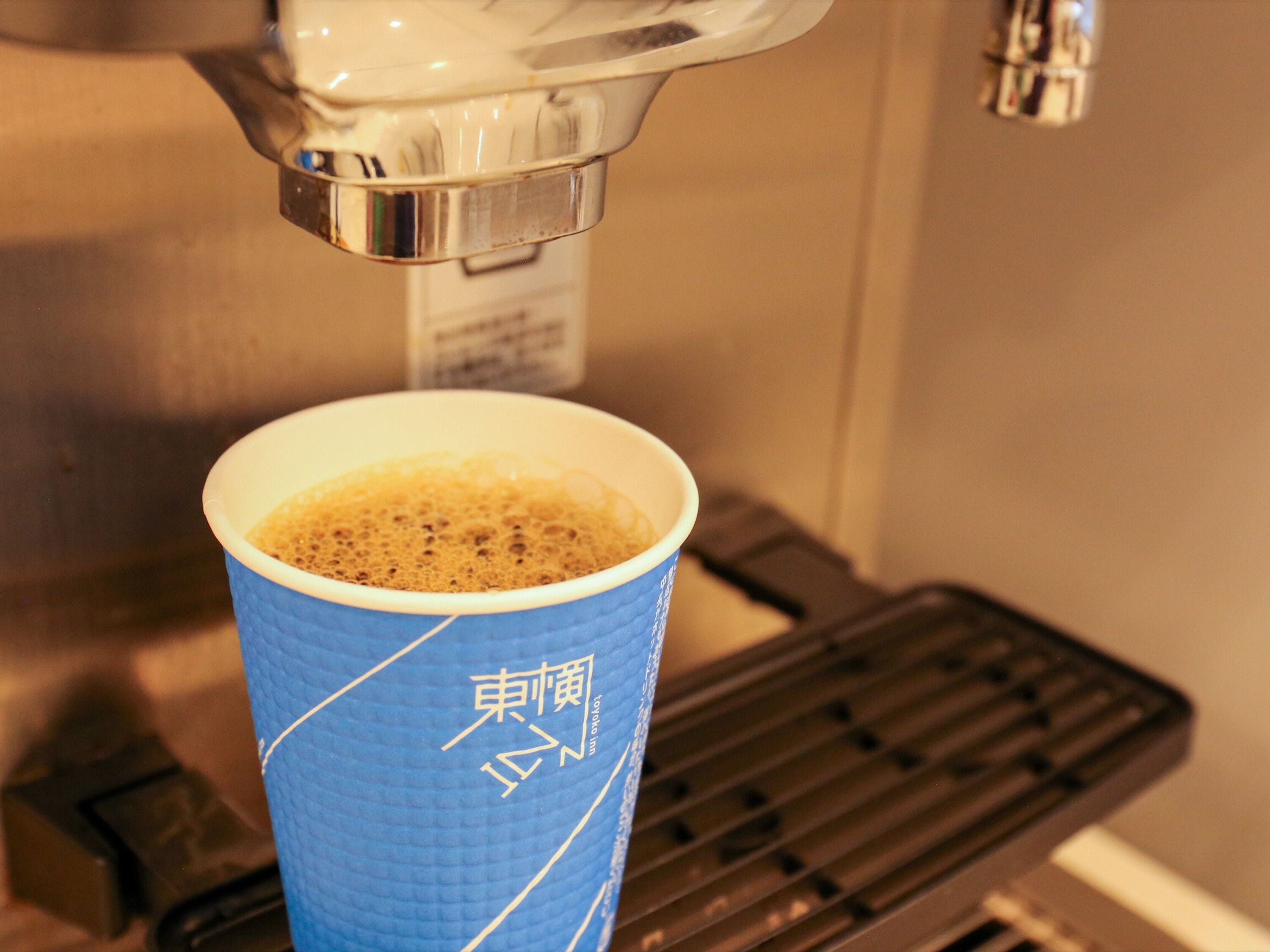 A paper cup with Japanese characters and a coffee machine dispensing coffee into it.