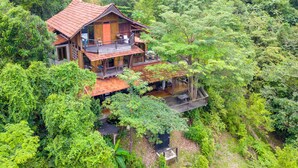 A multi-story wooden house surrounded by dense forest. - Spyder Hill (Seremban)