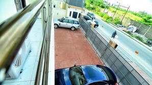 A view from a window overlooking a parking area with a car parked in the foreground and a street with parked cars and a person walking in the background. - Madiba Court (Lekki)