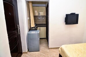 A compact room with a bed, a small kitchenette with a refrigerator, and a mounted television. - Madiba Court (Lekki)