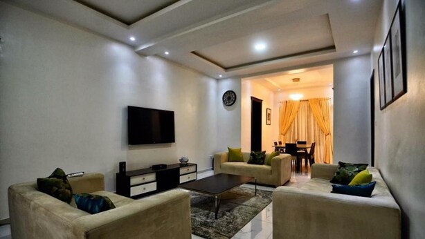 A living room with a flat-screen TV, two sofas, a coffee table, and a dining area with a table and chairs. - Madiba Court (Lekki)
