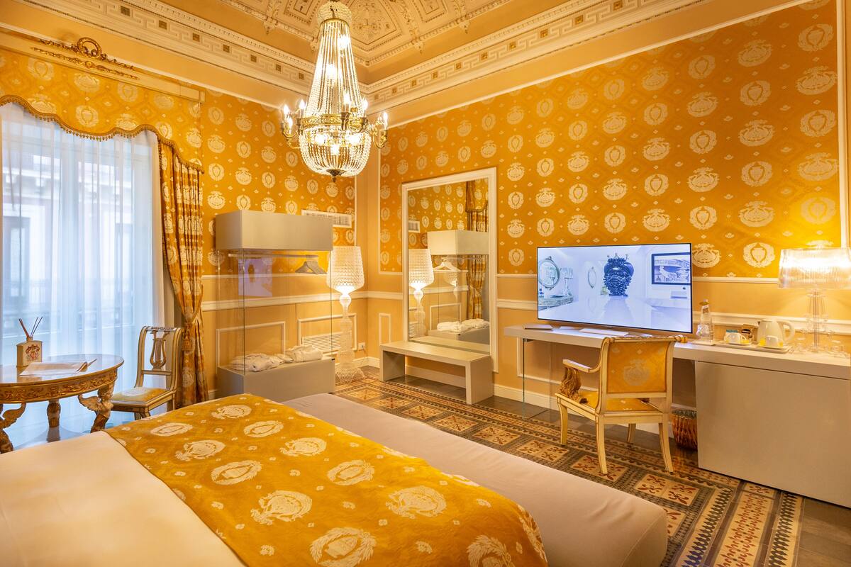 A hotel room with a large bed, a desk, a television, and a chandelier.