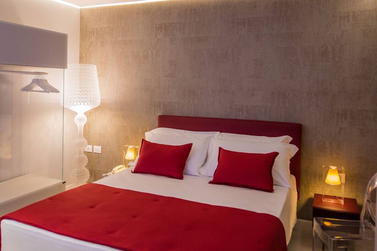 A modern hotel room with a large bed, red and white bedding, a marble floor, and a wall-mounted TV.