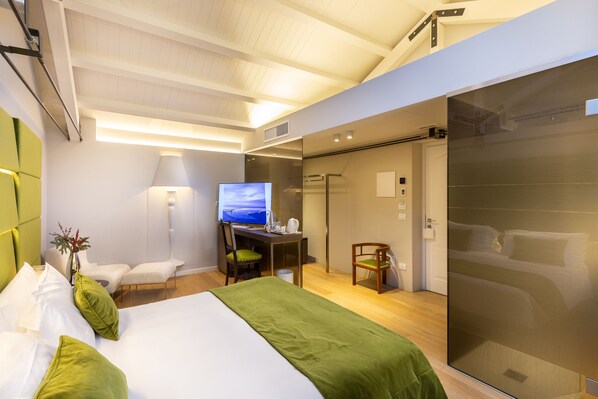 A modern hotel room with a bed, a desk with a computer, a TV, and a sliding door to a bathroom.