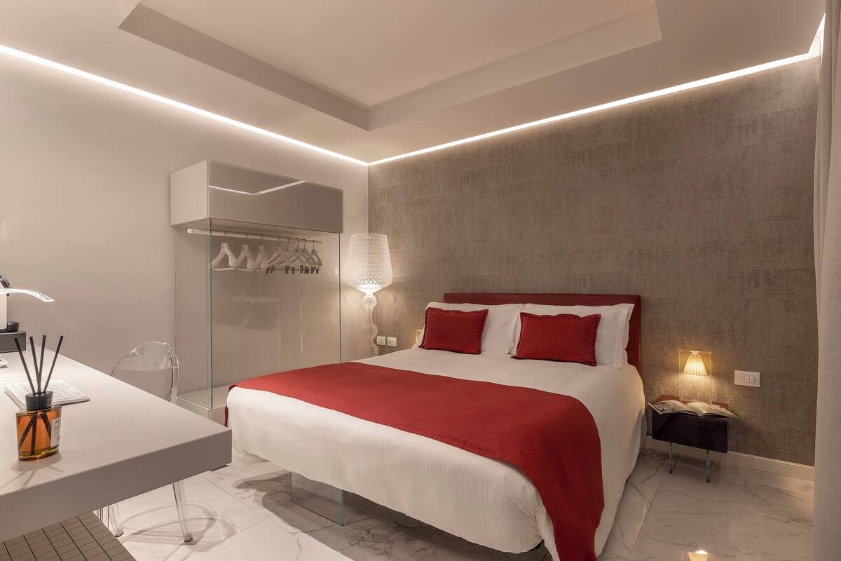 A modern bedroom with a large bed, bedside tables, a desk, and a mirror.