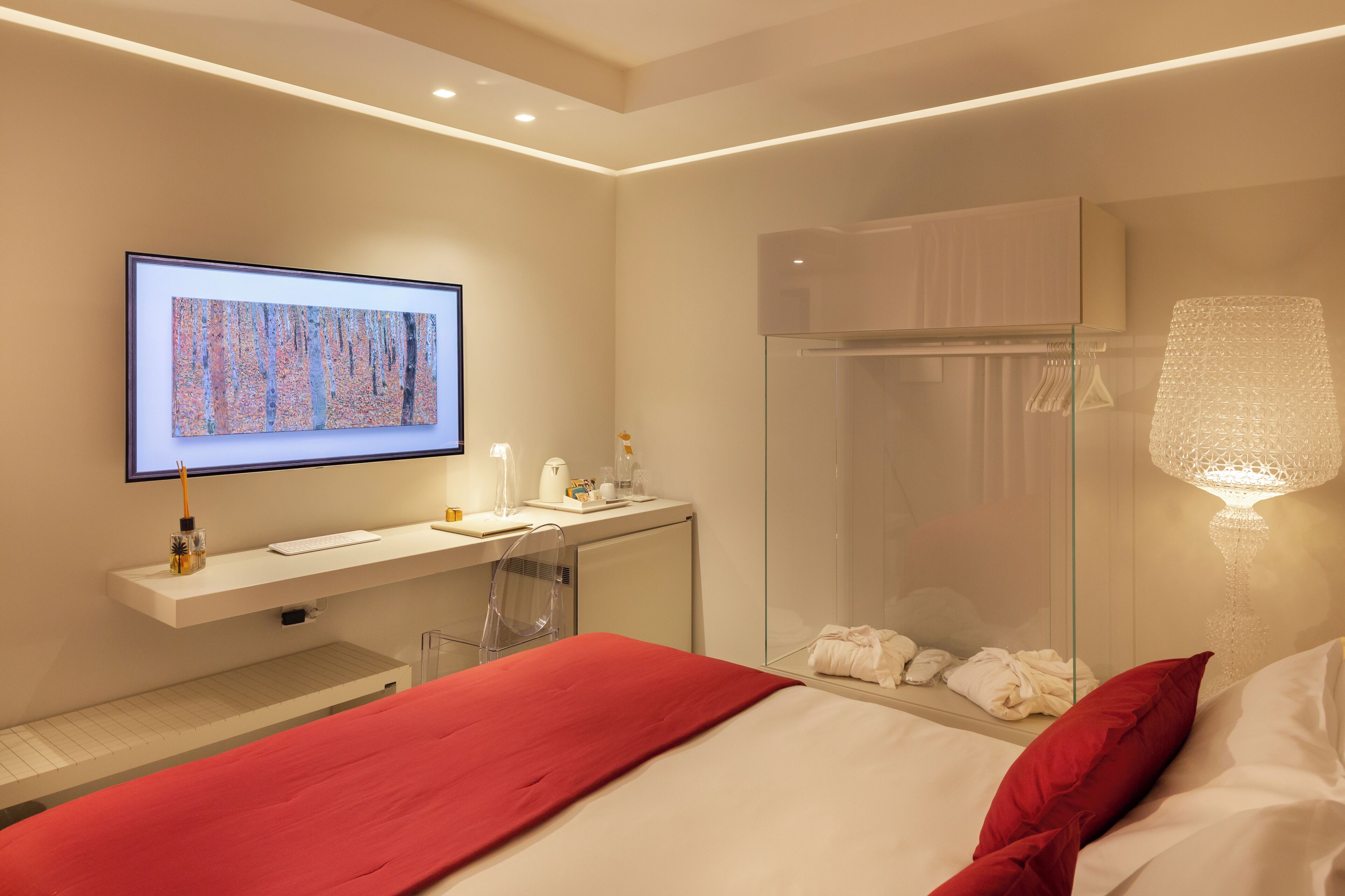 A modern hotel room with a bed, a desk with a computer, a shower, and a large artwork on the wall.