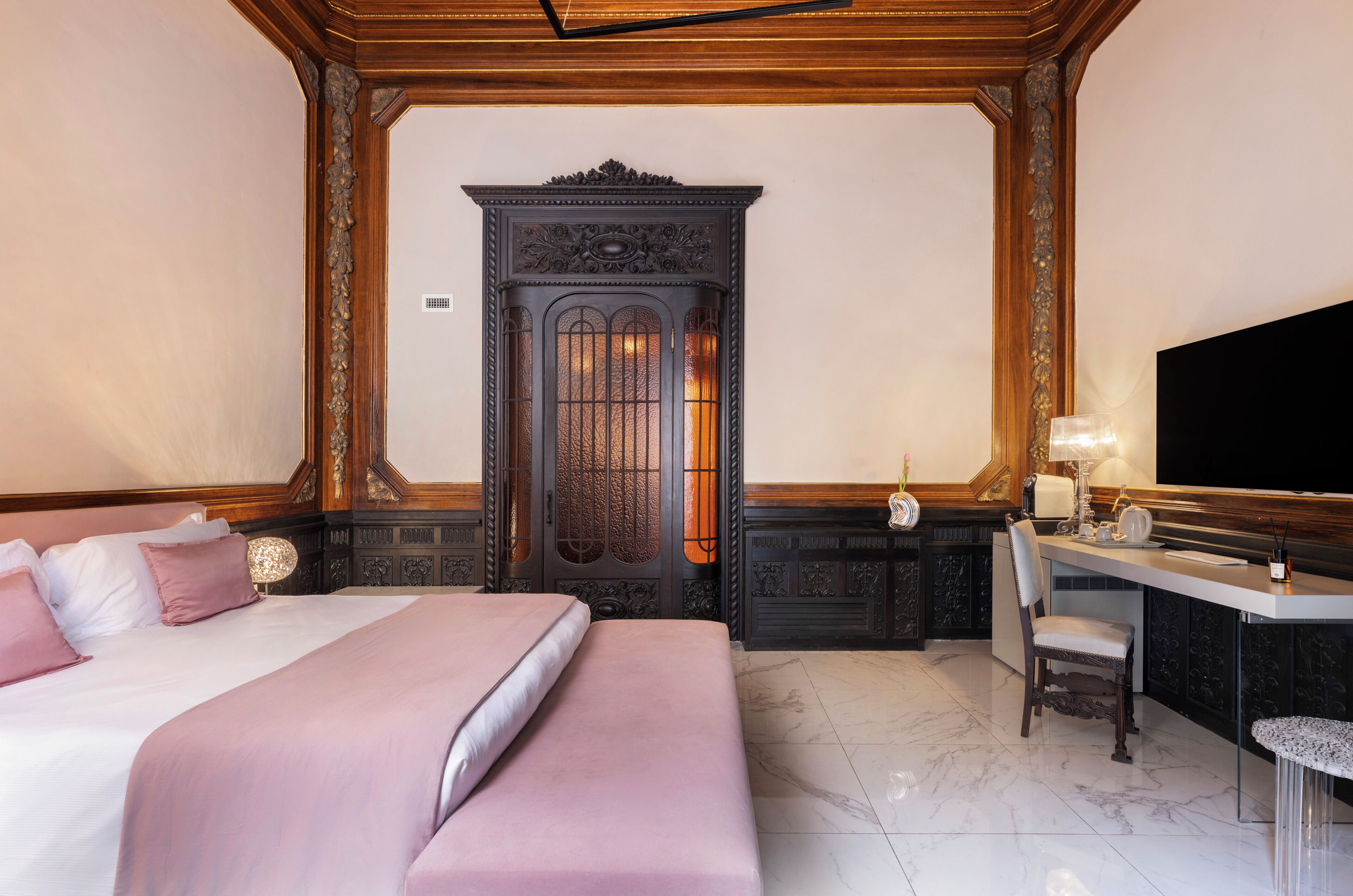 A hotel room with a bed, a desk with a chair, a television, and a decorative cabinet.