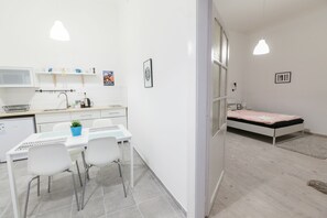 Una habitación moderna y minimalista con kitchenette, un comedor con mesa y sillas, y una cama individual.