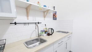 A modern kitchen with white cabinets, a stainless steel sink, and a wooden countertop. There are shelves above the sink holding various items, and a coffee machine is visible on the countertop. - Classic Ernesto near Opera (Budapest)