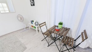 A compact living space with a wooden table, a small white shelf with books and a picture frame, a standing fan, and a green plant. - Classic Ernesto near Opera (Budapest)
