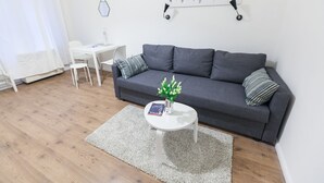 A modern living room with a grey sofa, a white coffee table, and a small white table. There is a wall-mounted artwork above the sofa and a white curtain partially covering a window. - Classic Ernesto near Opera (Budapest)