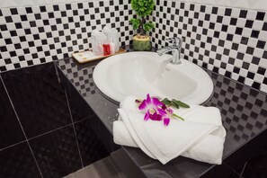 A bathroom with a checkered black and white tiled wall, a white sink, and a small potted plant.