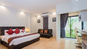 A modern hotel room with a large bed, a sofa, a desk, and a view of greenery through the window. - Journey Residence Phuket  (Choeng Thale)