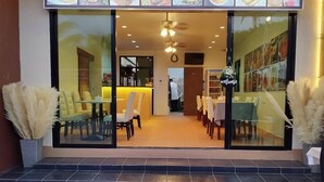 A restaurant with a glass facade, yellow chairs, and a 'Welcome' sign. - Journey Residence Phuket  (Choeng Thale)